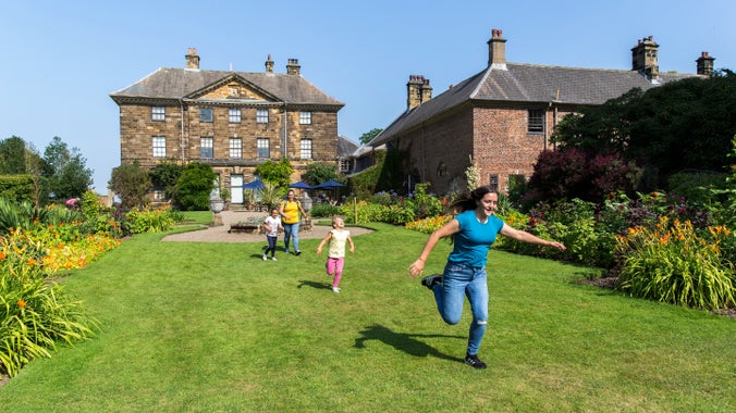 Young family running through the south facing formal gardens in front of Ormesby Hall